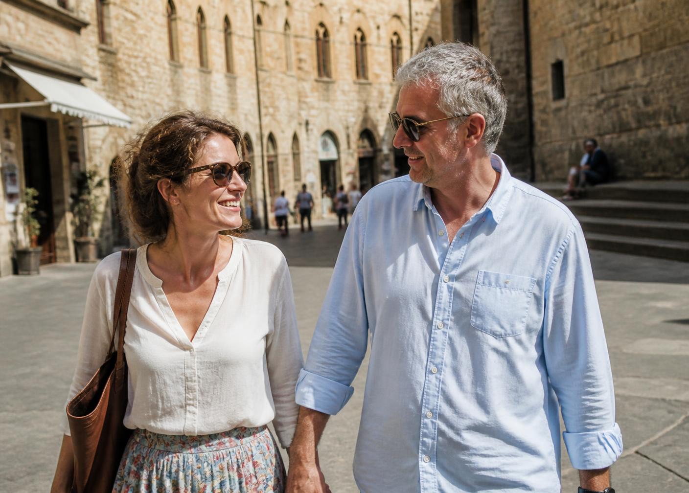 Una donna e un uomo intorno ai cinquant'anni camminano sorridendo in una piazza di un centro storico italiano